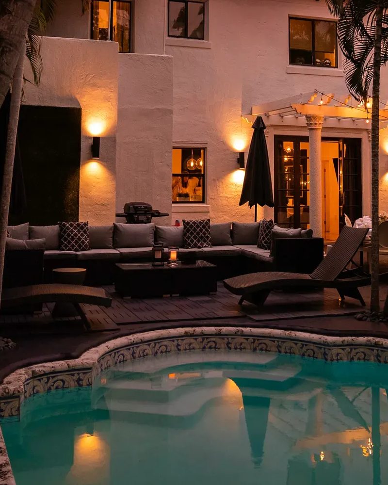 A private villa courtyard at dusk with a lit pool, lounge seating, and string lights